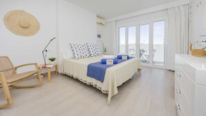 Een slaapkamer met een bed, een schommelstoel, een klein tafeltje met een plant en uitzicht buiten door een schuifdeur.