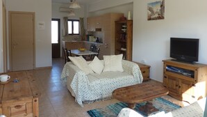 Una sala de estar con sofá, mesa de centro, mueble para televisión y una cocina al fondo.