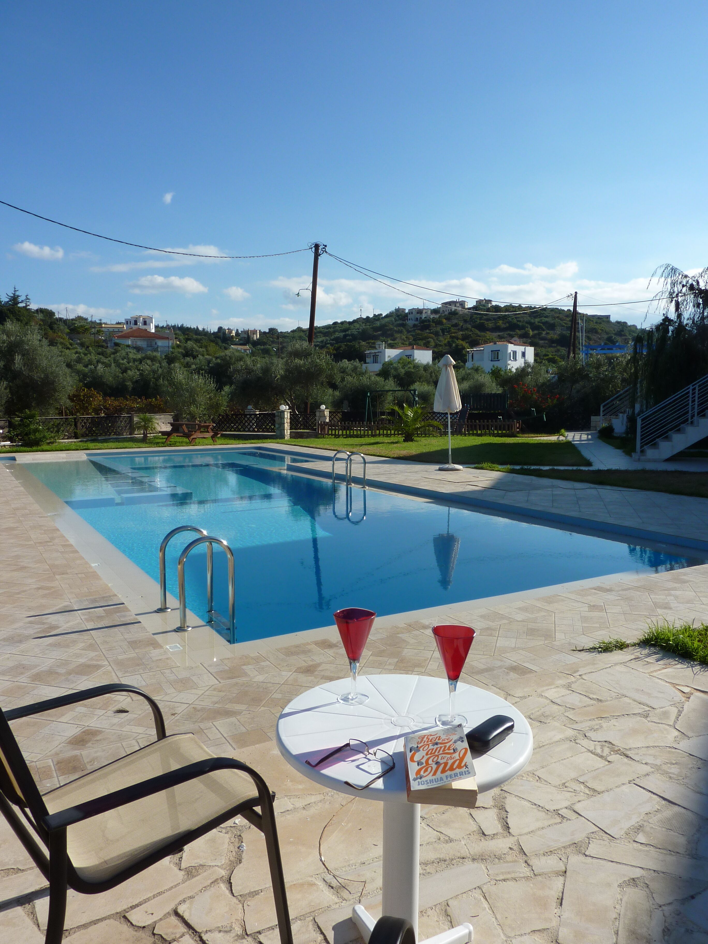 Una piscina con zona de patio, una mesa con un libro y vasos, y una silla.
