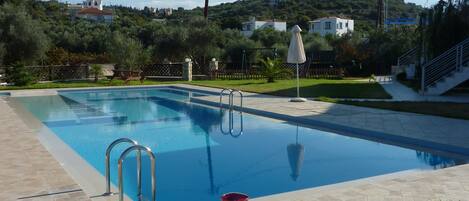 Una piscina con zona de patio, una mesa con un libro y vasos, y una silla.