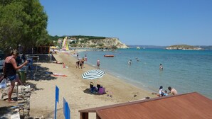 A beach with clear skies, people swimming, and a sandy shore.
