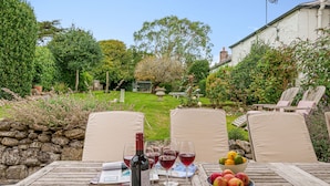 A wooden table with wine glasses, a bottle, and a bowl of fruit in a garden setting. - Albury House -  Charmouth, Lyme Regis (Charmouth)