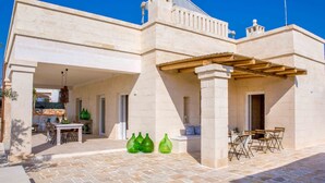 Ein Gebäude mit einer Steinfassade, einem überdachten Patio mit Tisch und Stühlen sowie einer kleinen, durch eine offene Tür einsehbaren Küche.