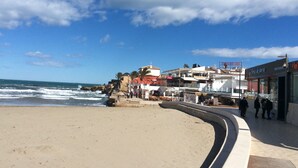 A beach with a curved walkway, rocky shoreline, and buildings with shops and restaurants. - Modern Ground Floor Apartment, Minutes walk from the Arenal beach (Platja de L'arenal)