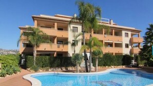 A multi-story hotel with a swimming pool, palm trees, and a clear blue sky. - Modern Ground Floor Apartment, Minutes walk from the Arenal beach (Platja de L'arenal)
