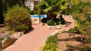 A pathway leading to a pool surrounded by lush greenery and palm trees, with buildings in the background. - Modern Ground Floor Apartment, Minutes walk from the Arenal beach (Platja de L'arenal)