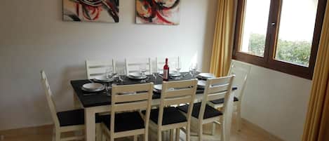 A dining area with a table set for six, white chairs, and two abstract paintings on the wall.