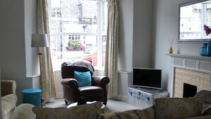 Ein Wohnzimmer mit Sofa, Sessel, Fernseher und Kamin.