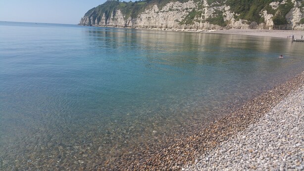 Ein Kieselstrand mit klarem Wasser und felsigen Klippen.