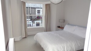 Ein Hotelzimmer mit einem großen Bett, einem Nachttisch mit Lampe und einem Fenster mit Blick zum Hauseingang des Hotels.