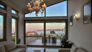 En rummelig opholdsstue med en stor skydedør, der fører til en balkon med en betagende udsigt over havet og bjergene.