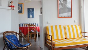 A living room with a striped sofa, a wicker chair, a dining table with a red tablecloth, and a framed picture on the wall. - Comfortable apartment, very quiet, superb sea view, sleeps 4/6 (Cadaqués)