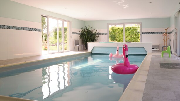 Une piscine intérieure à l’eau claire, un flotteur en forme de flamant rose et une chaise verte.