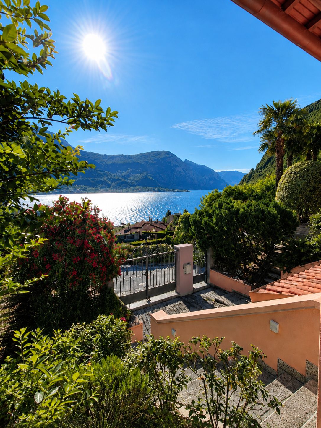 A terrace with a view of a lake and mountains, surrounded by lush greenery and a clear sky.