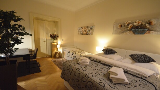 Une chambre d’hôtel avec un lit, une table à manger et une chaise. Il y a un tableau au mur et une plante dans un coin.