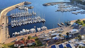 En lystbådehavn med mange både i havnen, en buet bølgebryder og frit udsyn over det omkringliggende landskab, inklusive fjerne bjerge og en lille ø.