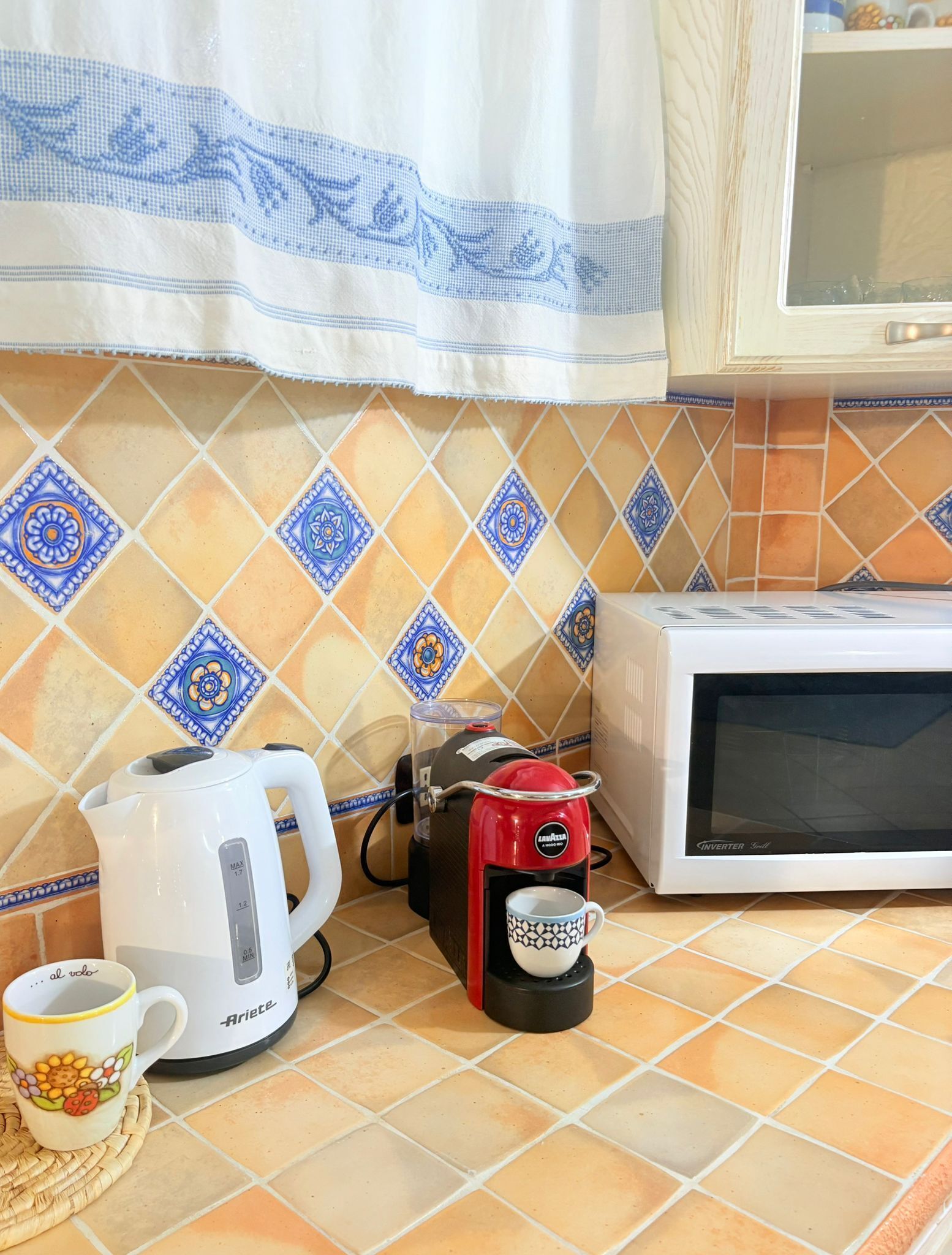 A kitchen with a coffee maker, kettle, and microwave on a tiled countertop.