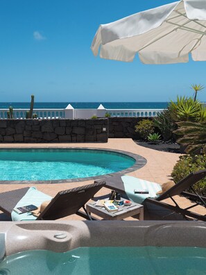 Un espace aménagé au bord de la piscine, avec des chaises longues, un jacuzzi et une vue sur l’océan.