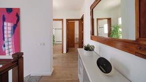 Een gang met een houten vloer, een witte console tafel met een plant erop, en een grote spiegel.