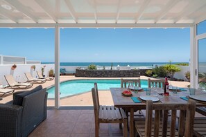 Un espace extérieur abrité comprenant une piscine, des chaises longues et une table dressée pour les repas.