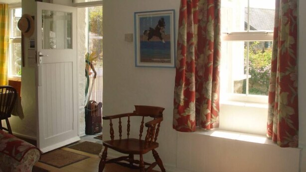 Une pièce avec une chaise en bois, une porte, une fenêtre avec des rideaux et un tableau encadré accroché au mur.