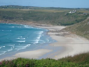 A coastal landscape with a sandy beach, rocky shoreline, and distant houses. - At the very end of Cornwall , charming fisherman's cottage (Sennen)