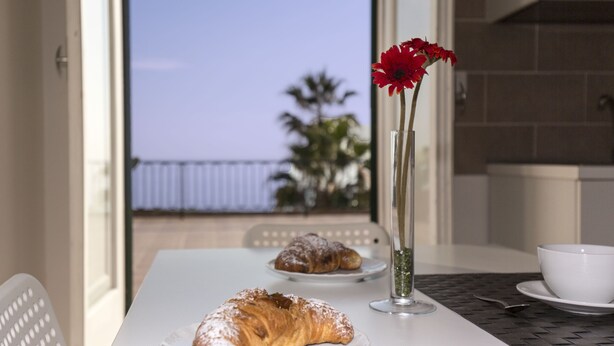 A table with croissants and a vase with a flower, a white bowl, and a spoon on a table with a view of the sky and a balcony. - House with Big Terrace in Seaside, Syracuse - Ortigia (Siracusa)
