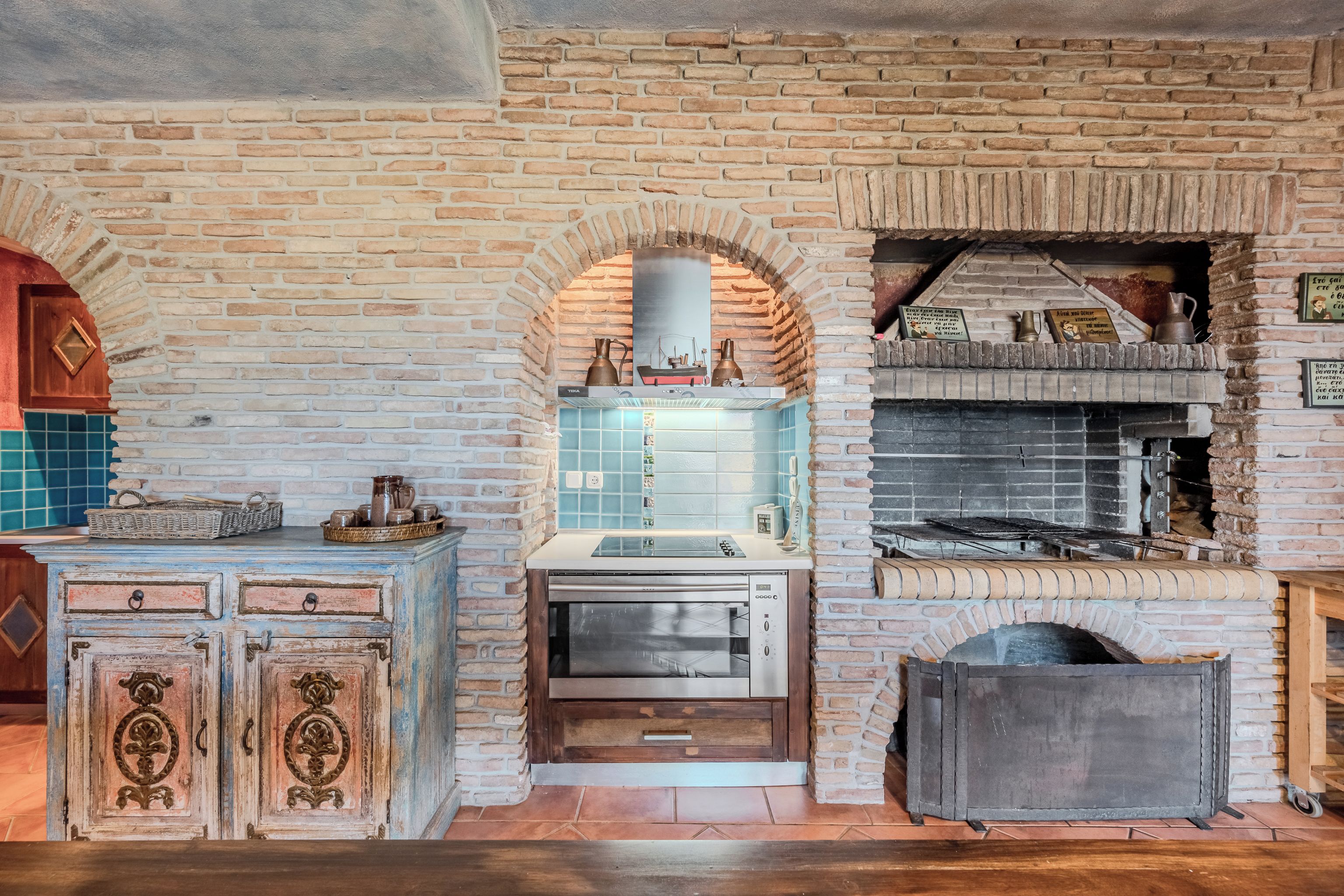 A kitchen with a brick wall, a built-in oven, and a wooden cabinet with drawers.