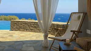 A seaside patio with stone flooring, white curtains, and flags.