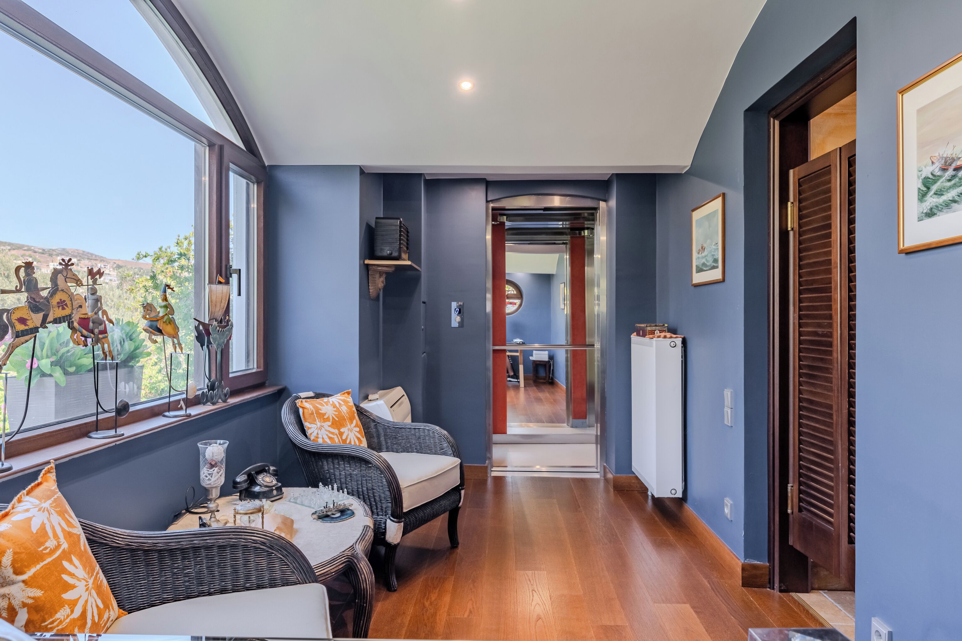A room with a view of the outdoors, a dining area with wicker furniture, and a hallway leading to another room.