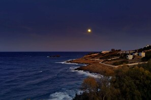 A coastal landscape with a clear view of the sea, a small rocky outcrop, and a few buildings on the hillside. - Villa Scorpio, Seafront Luxury & Infinity Pool (LAVRIO)