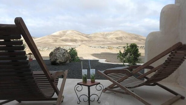 Una terraza con dos sillones de madera y una pequeña mesa con bebidas, con vista a un paisaje desértico.