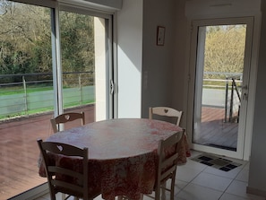 A dining area with a table and chairs, large windows, and a view of a green outdoor area.