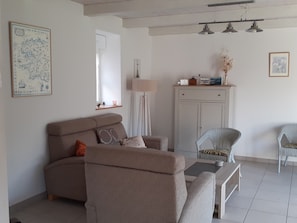 A living room with a sofa, armchair, and a small table. There is a cabinet with a mirror and a lamp.