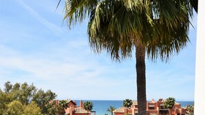 Terrassa amb taula preparada per a dos, amb vista a una zona costera amb edificis i palmeres.