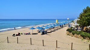 Una platja amb files de papereres blaves, una torre de socorristes i un mur de pedra amb vegetació.