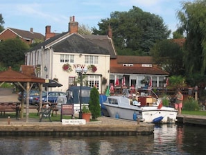 A riverside building with a sign reading 'NEW' and a dock with boats.