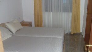 A single bed with a wooden frame, a nightstand, and a window with curtains.