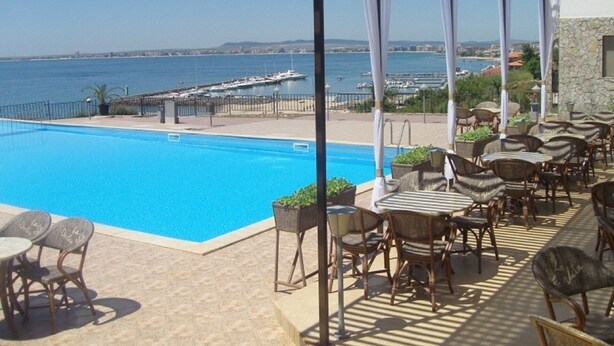 A poolside area with a view of the sea, outdoor seating, and a covered section with umbrellas.