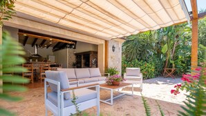 An outdoor patio with a covered seating area, a dining table, and a kitchen visible through an open door.