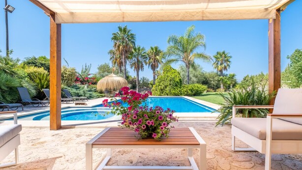A poolside area with lounge chairs, a table with flowers, and a view of the pool and palm trees.