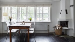 Uma sala de jantar com mesa e cadeiras, uma janela com cortinas, uma lareira e um radiador.