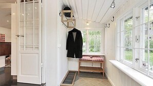 Um quarto com uma janela grande, um banco com almofada xadrez e um casaco pendurado em um cabide.
