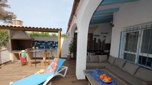 A patio with a blue lounge chair, a table with oranges, and a barbecue area. - CASA MARINERA,Ideal house for your holidays near the sea, free wifi, optional air conditioning, private pool, pets allowed, dog’s beach (Delta de l'ebre)