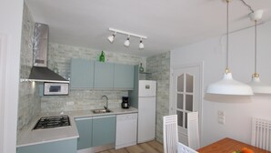 A compact kitchen with a microwave, stove, and dishwasher. There is a dining table with chairs and a fruit bowl. - CASA MARINERA,Ideal house for your holidays near the sea, free wifi, optional air conditioning, private pool, pets allowed, dog’s beach (Delta de l'ebre)