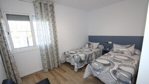 A room with two beds, a window with curtains, a bedside table, and a chair. - CASA MARINERA,Ideal house for your holidays near the sea, free wifi, optional air conditioning, private pool, pets allowed, dog’s beach (Delta de l'ebre)