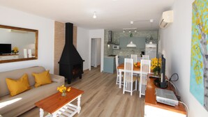 A modern living room with a sofa, coffee table, and fireplace. There is a dining area with a table and chairs. The kitchen is visible in the background with a window and cabinets. - CASA MARINERA,Ideal house for your holidays near the sea, free wifi, optional air conditioning, private pool, pets allowed, dog’s beach (Delta de l'ebre)