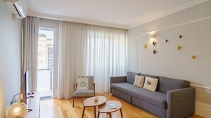 A modern living room with a grey sofa, two round wooden tables, a TV, and a large window with curtains. - Feel Porto Downtown Charming Apartment I (Oporto)
