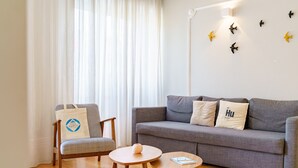 A living room with a grey sofa, a wooden chair, two small round tables, and a white wall with bird wall art. - Feel Porto Downtown Charming Apartment I (Oporto)