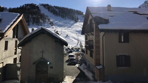 Un village enneigé avec une église, une piste de ski en arrière-plan et un ciel dégagé.